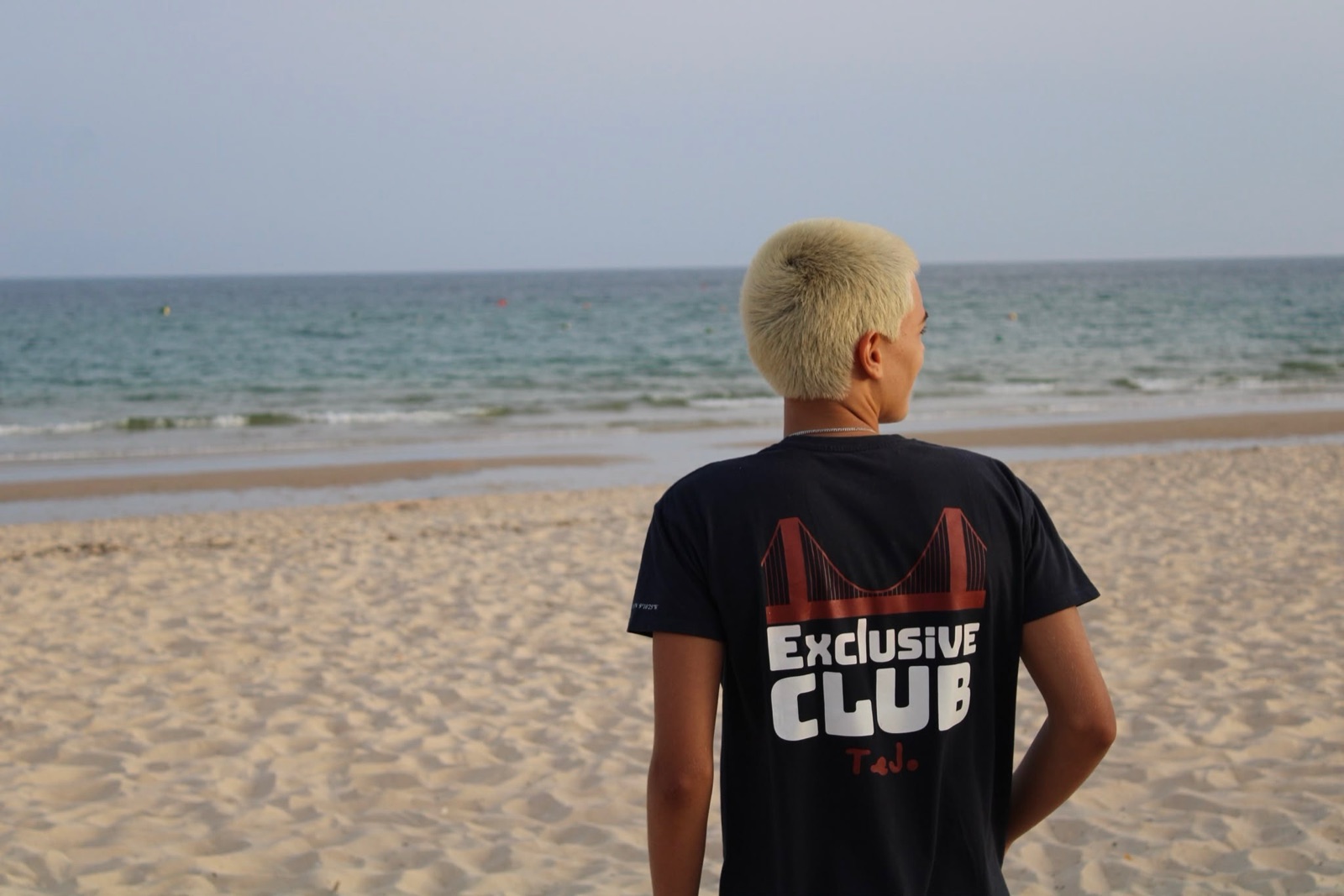 The Exclusive Club tee on the beach, seen from behind, showing the 25 de Abril bridge graphic.